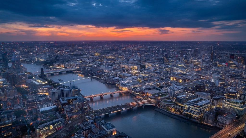 Aerial view of London and the Thames at dusk, with the city lit beneath an orange sky