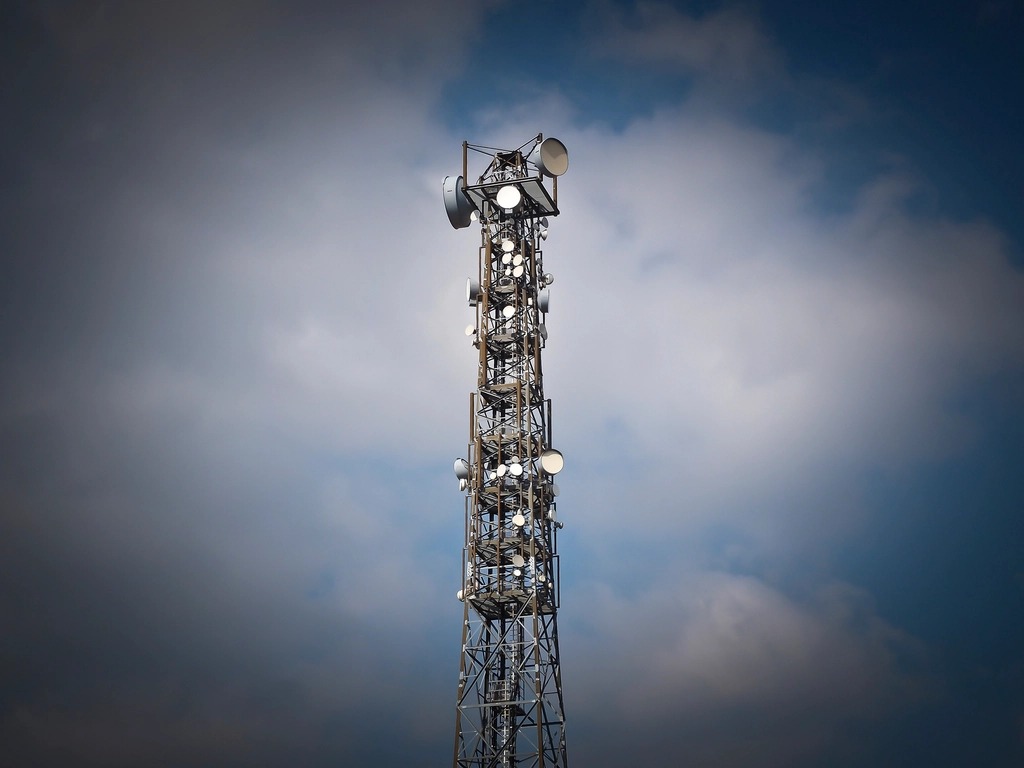 A mobile network mast seen from below against a clouded sky